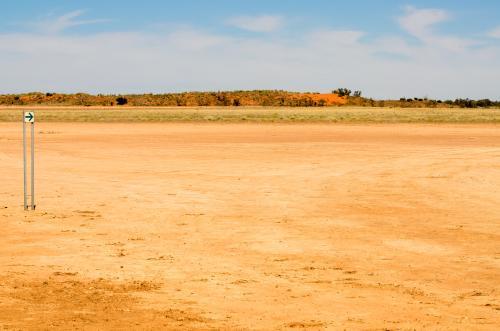 Direction arrow on a desert claypan with red sand dunes in the distance - Australian Stock Image