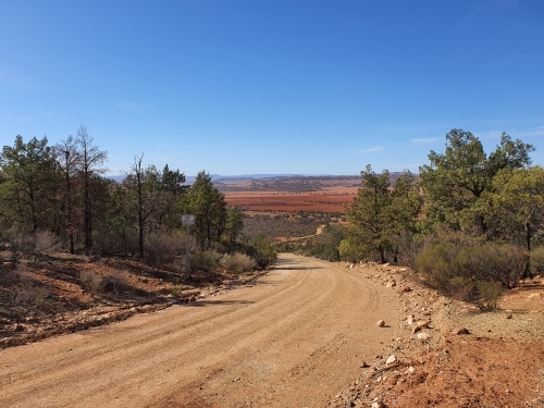 dirt road leading down hill to brown plains - Australian Stock Image