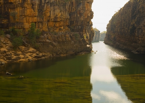 Distant canoeists on still water in deep gorge with cliffs - Australian Stock Image