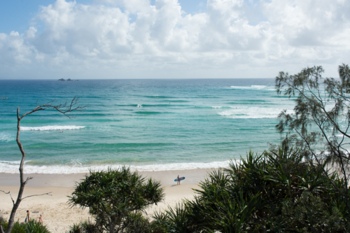 Distant shot of surfer with board walking along beach with ocean in background - Australian Stock Image