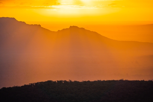 Distant view of a dramatic golden sunset over mountains with rayls of light - Australian Stock Image