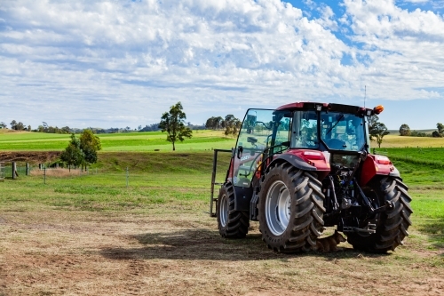 Dog resting in shade under tractor in paddock - Australian Stock Image