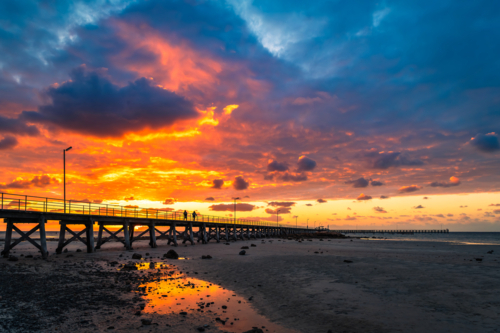 Dramatic sunset above Moonta Bay Jetty with people walking along,  Copper Coast, Yorke Peninsula - Australian Stock Image