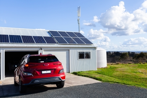 Driving electric vehicle car into solar and wind powered shed on country farm  - living sustainably - Australian Stock Image