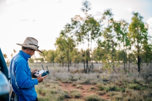 Drone operator looking at remote control in the paddock - Australian Stock Image