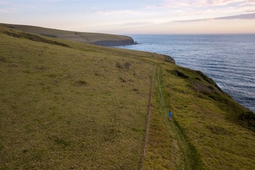 Drone Shot of Man Running on Headland Overlooking Ocean - Australian Stock Image