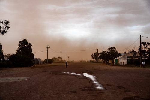 Dust storm hitting small remote town with a child riding a bike on the road - Australian Stock Image