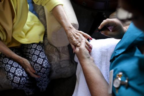 Elderly lady having nails painted by carer at nursing home - Australian Stock Image