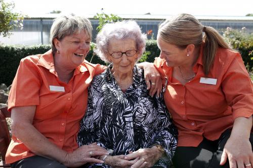Elderly lady sitting outside between two carers at aged care facility - Australian Stock Image