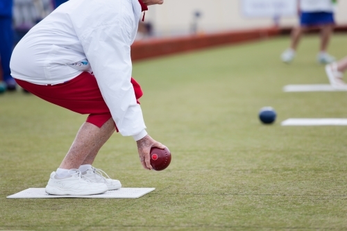 Elderly woman crouching before delivering a lawn bowl - Australian Stock Image