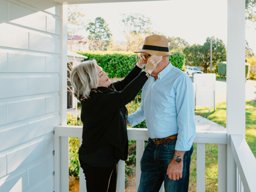 Elderly woman fixing the hat of an elderly man on the porch. - Australian Stock Image