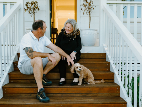 Elderly woman sitting next to a middle-aged man and small dog in the porch. - Australian Stock Image