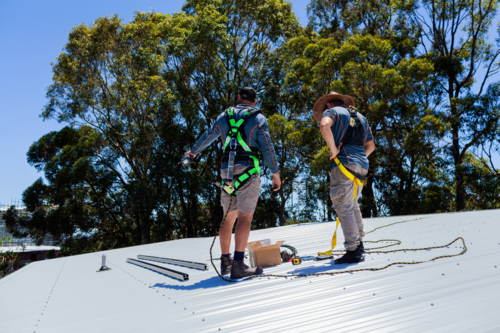 Electrician tradesmen workers on house roof discussing installing solar panel system together - Australian Stock Image