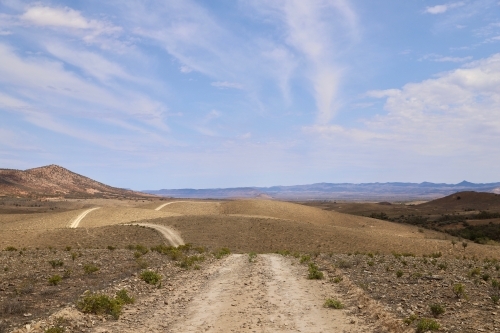 Empty dirt road across dry plains on a sunny day - Australian Stock Image