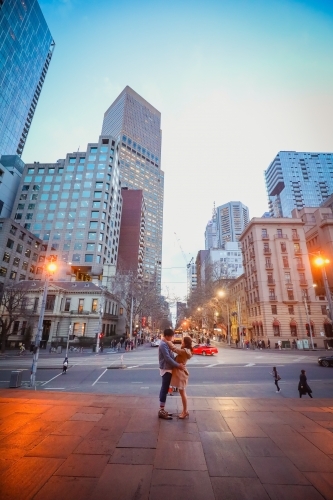Engaged couple embracing in the city with Melbourne cityscape in background at night - Australian Stock Image