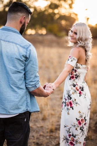 Engaged couple holding hands while man looks down at engagement ring - Australian Stock Image