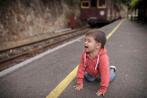 Excited 2 year old mixed race boy on hands and knees an a train platform - Australian Stock Image