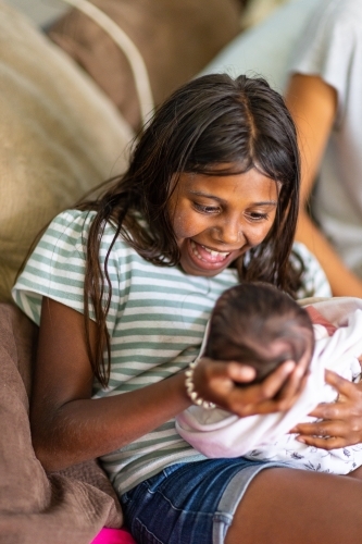 excited young girl holding her newborn baby sister - Australian Stock Image