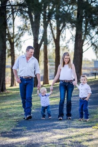 Family holding hands of young children walking down path - Australian Stock Image