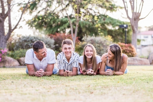 Family of four lying on grass mum and dad looking at children happy - Australian Stock Image