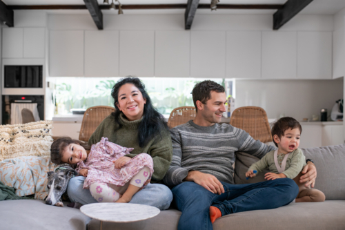 Family of Four Sitting Together on Couch in Living Room - Australian Stock Image