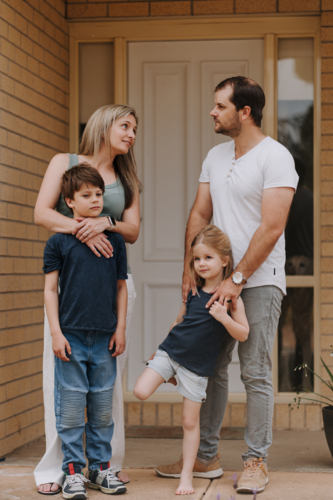 Family of four standing in front of their house. - Australian Stock Image