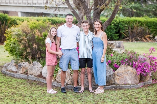 Family of four standing together in garden smiling - Australian Stock Image