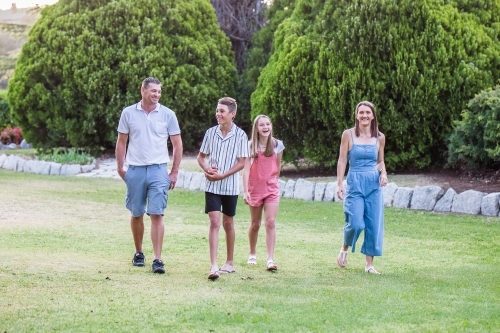 Family of four walking together talking in garden laughing - Australian Stock Image