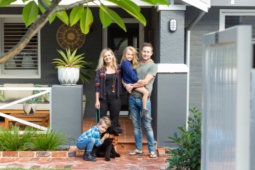 Family of four with pet dog in front of suburban home - Australian Stock Image