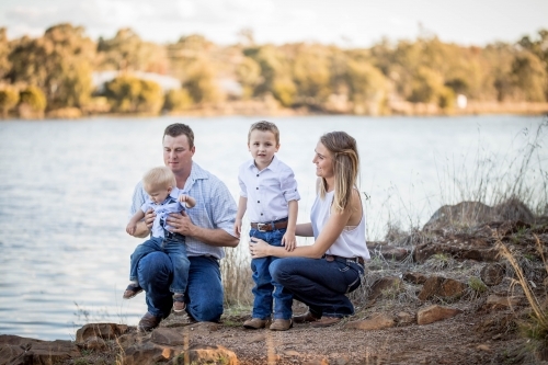 Family of husband and wife with two sons kneeling down near water
