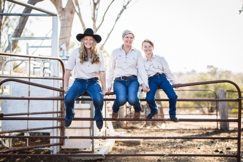 Family of three sitting on gate in stock yards on farm in drought - Australian Stock Image