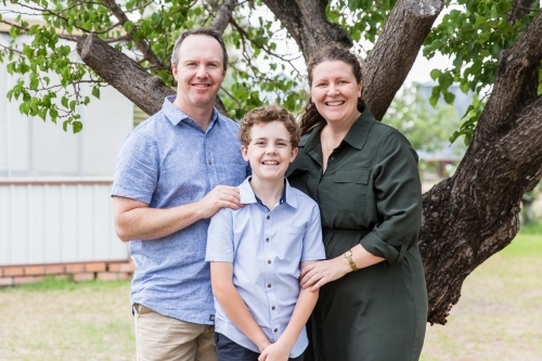 Family of three standing together in back yard at home smiling - Australian Stock Image