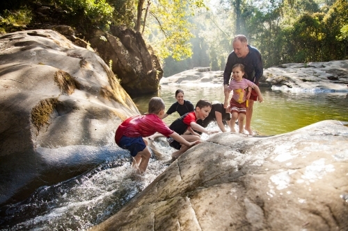 Family playing on rocks and in river water at ladies well - Australian Stock Image