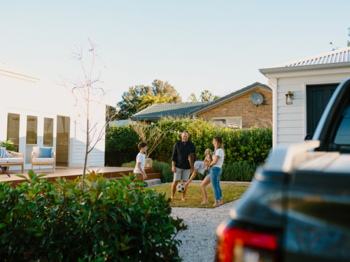 Family playing with a soccer ball in their yard. - Australian Stock Image