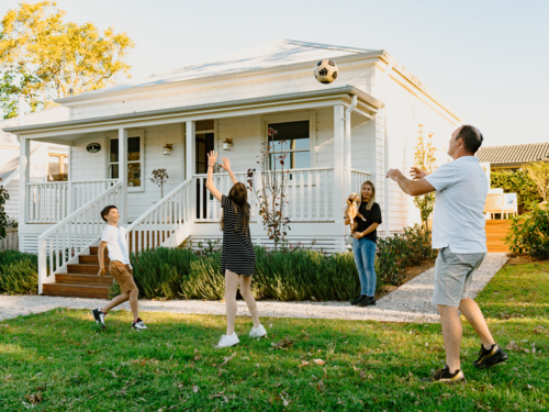 Family tossing a soccer ball inside their yard. - Australian Stock Image