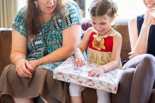 Family unwrapping Christmas gifts together, little girl with big gift - Australian Stock Image