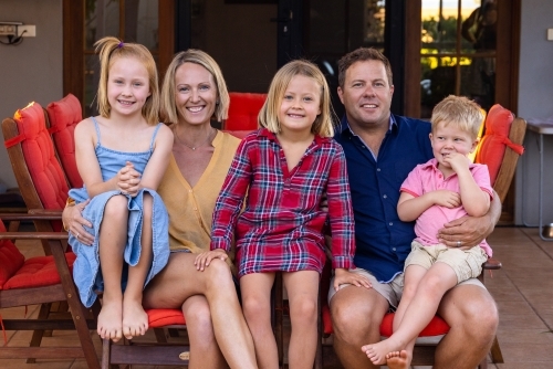 family with three young children sitting outside their home - Australian Stock Image