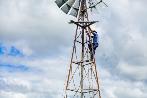 Farmer climbing up farm windmill to check and repair pump - Australian Stock Image