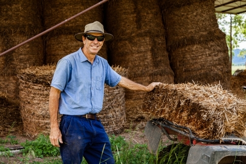 Farmer loading hay bale onto quad bike to feed livestock - Australian Stock Image
