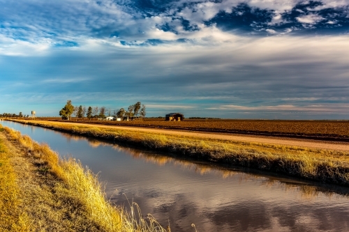 Farmland lining a straight river with farm house in distance - Australian Stock Image