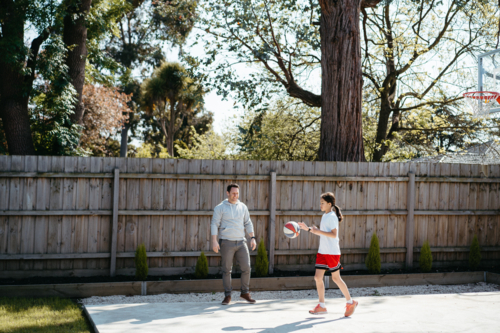 Father and daughter playing basketball in their yard. - Australian Stock Image