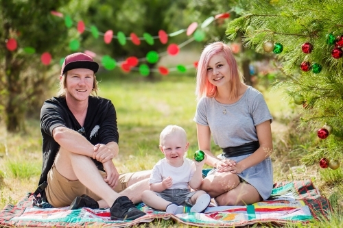 Father and mother sitting with child with Christmas decorations and trees - Australian Stock Image