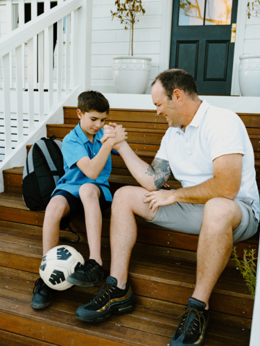 Father and son doing arm wrestling while sitting on the steps of their house. - Australian Stock Image