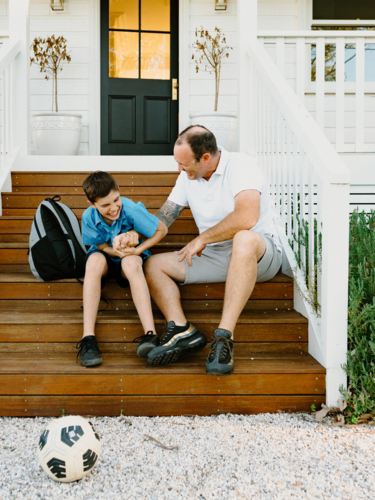 Father and son doing arm wrestling while sitting on the steps of their house. - Australian Stock Image