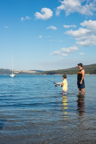 Father and son fishing in the water at beach - Australian Stock Image