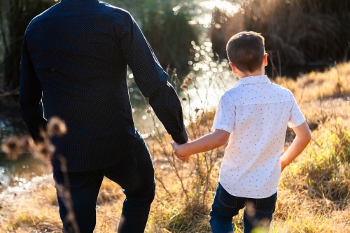 Father and son holding hands on an adventure through the grass - Australian Stock Image