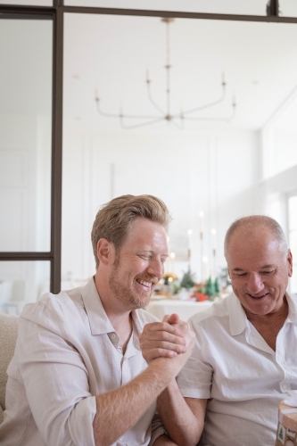 Father and son holding hands sitting together at home - Australian Stock Image