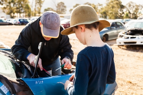 Father and son in wreckers pulling apart smashed car for parts - Australian Stock Image