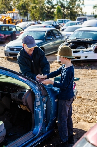Father and son in wreckers pulling apart smashed car for parts - Australian Stock Image