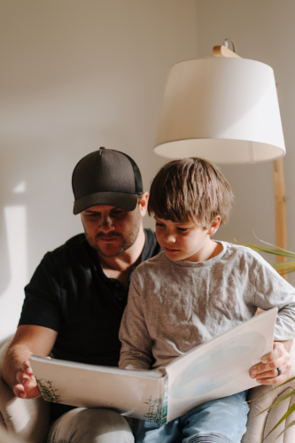 Father and son looking at an album while sitting on the couch. - Australian Stock Image